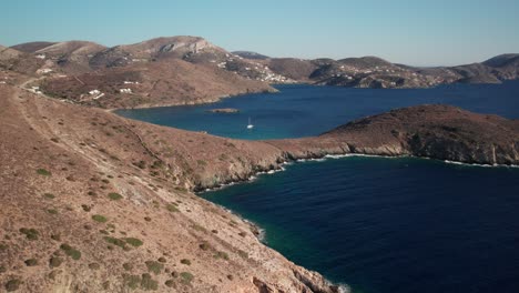 Drone-trucking-pan-of-syros-greece-coastline,-deep-blue-water-contrasting-tan-dry-mountainous-landscape