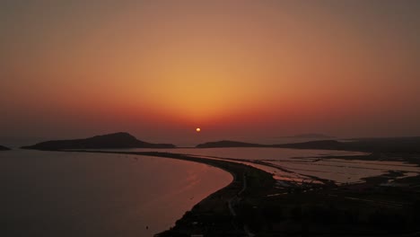 Die-Drohne-Senkt-Sich-Rückwärts,-Während-Der-Sonnenball-Ein-Rot-orange-gelbes-Leuchten-In-Den-Himmel-über-Pylos-In-Griechenland-Wirft