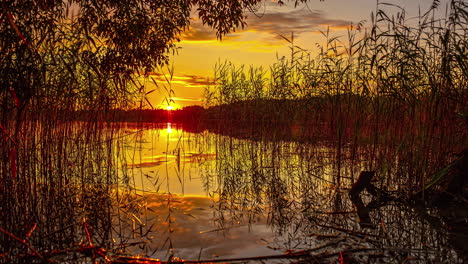 Cinematic-time-lapse-of-the-sunset-behind-a-lake-with-beautiful-coulds-in-the-sky-and-grass-in-the-front
