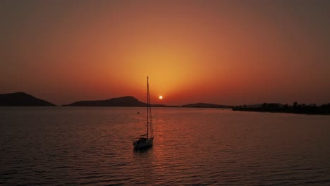 Aerial-orbit-around-anchored-sailboat-in-open-ocean-off-coast-of-pylos-greece,-sunset-sky