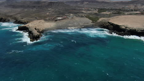 Vista-Aérea-A-Lo-Lejos-Y-En-Círculo-Sobre-La-Playa-De-La-Pared-Y-La-Formación-Rocosa-Que-Hay-Allí,-En-La-Isla-De-Fuerteventura-En-Un-Día-Soleado