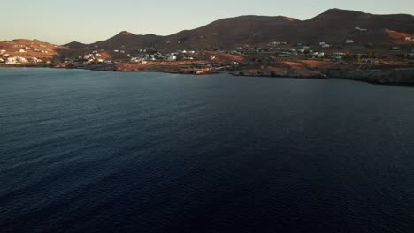 Drone-dolly-tilt-up-to-coastal-town-of-syros-greece-at-sunset,-space-for-text