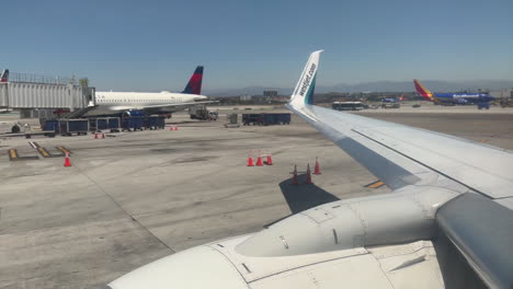 Pan-Up-From-WestJet-737-Airplane-Engine-to-Wing,-While-Parked-at-LAX-Airport-with-Other-Airplanes-in-Background,-from-a-Window-Seat-Point-of-View,-on-7-13-2023