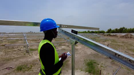 Schwarzafrikanischer-Ingenieur-Mit-Blauem-Helm,-Der-Messungen-Der-Neigungswinkel-Der-Solarpanel-Array-Strahlstruktur-Durchführt