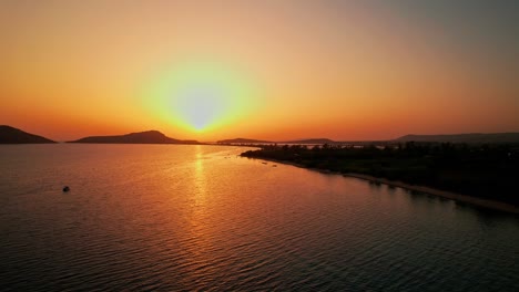 Large-yellow-ball-of-sun-spreads-golden-red-hue-gradient-light-throughout-ocean-and-sky,-pylos-greece