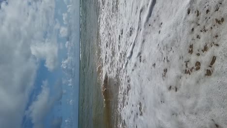 VERTICAL-Slow-motion-Tropical-ocean-waves-flowing-over-golden-sandy-beach-under-blue-cloudy-sky