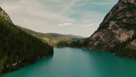 Drone-flyover-shot,-over-a-turquoise-mountain-lake,-between-tall-mountains-on-a-sunny-day