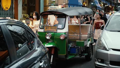 Tuk-Tuk-Taxi-in-the-city-of-Bangkok,-Thailand-driving-through-a-full-street-of-people,-restaurants-and-shops