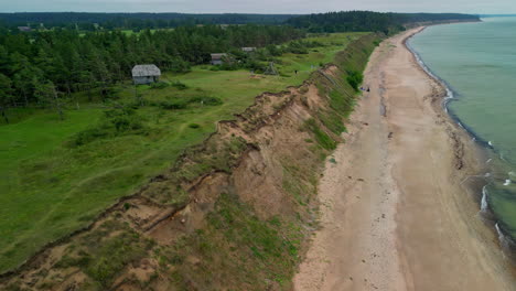 Drone-footage-of-a-coastline-with-houses-on-a-ridge-next-to-a-vast-sandy-beach