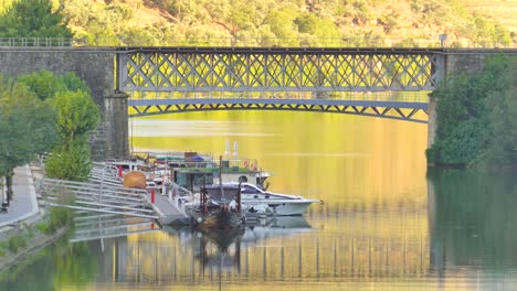 Boats-Docked-In-Front-Of-An-Iron-Bridge-Across-Douro-River-In-Pinhao,-Portugal