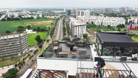 Aerial-drone-camera-moving-backwards-showing-an-aerial-view-of-Rajkot-and-a-terrace-garden-on-the-top-floor-of-a-high-rise-building