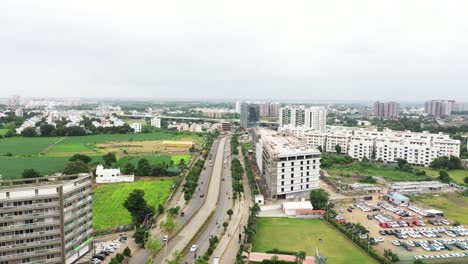Aerial-view-of-150-feet-ring-road-of-Rajkot-city,-lots-of-vehicles-plying-on-the-road-and-trees-planted-all-around-the-road