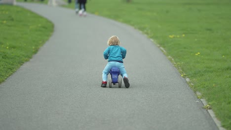 A-toddler-boy-rides-a-kickback-scooter-along-the-asphalt-path-in-the-park