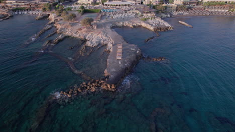 Aerial-drone-footage-post-sunset-over-a-Crete-town,-showcasing-its-rocky-coastline
