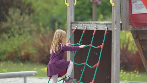 A-little-fair-haired-girl-climbs-a-jungle-gym-net-and-then-takes-a-slide-on-the-outdoor-playground