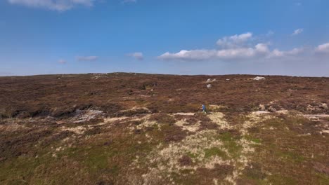 Tracking-drone-shot,-two-hikers-on-wild-moorland-trail,-sunny-day
