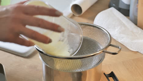 Person-pouring-thick-liquid-of-Smoothie-into-colander-in-kitchen,-close-up