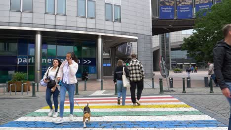 Menschen-überqueren-Den-Regenbogenfarbenen-Übergang-Vor-Dem-Gebäude-Des-Europäischen-Parlaments-In-Brüssel,-Während-Der-Bus-Vorbeifährt