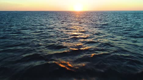 Aerial-dolly-push-in-tilt-up-to-setting-sun-over-ocean-ripple-texture