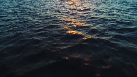 Deep-blue-last-light-of-dusk,-golden-hour-orange-yellow-on-ocean-ripple-wave-texture
