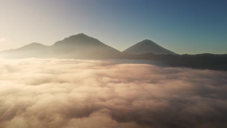 Aerial-view-over-valley-covered-in-fog-with-mountain-background,-sunrise-in-Bali,-Indonesia