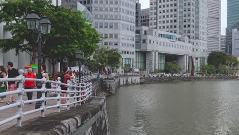 Los-Peatones-Caminan-A-Lo-Largo-Del-Muelle-De-Barcos-Con-Modernos-Rascacielos-Que-Bordean-El-Río-Singapur,-Singapur