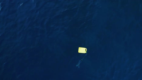 Yellow-gas-tank-and-weathered-rope-flotsam-debris-floats-in-ocean,-aerial-static-top-down-perspective
