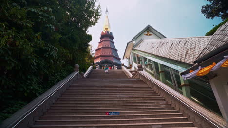 Woman-in-poncho-climbing-up-long-stairway-leading-to-pagoda,-Thailand