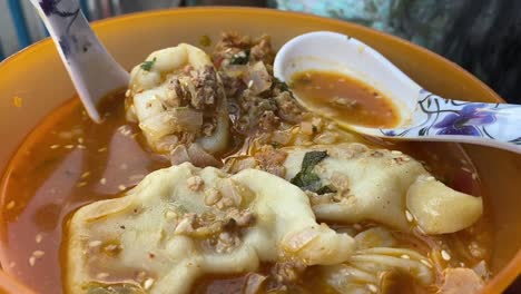 Very-close-up-shot-over-steamed-momo-in-spicy-soup-served-in-a-yellow-bowl-at-a-roadside-stall