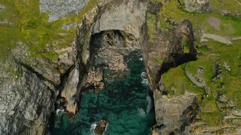 Beautiful-cinematic-aerial-shot-of-a-cave-near-the-ocean-in-the-summer