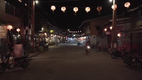 Hombre-Conduciendo-Scooter-En-Las-Calles-De-La-Ciudad-Iluminadas-Por-Linternas-En-La-Noche,-Tailandia