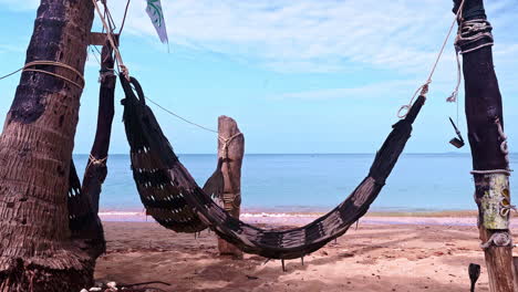 Woven-hammock-hanging-between-two-poles-on-tropical-beach-by-the-sea