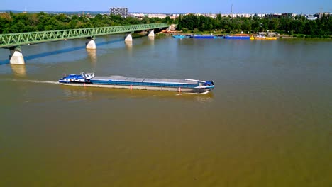 Freight-Barge-Cruising-In-The-Danube-River-Passing-Under-The-Truss-Railway-Bridge-In-Budapest,-Hungary