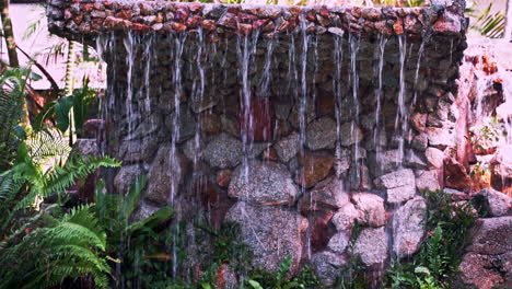 Rivulets-of-water-falling-to-garden-pond-from-carved-stone-slab-above