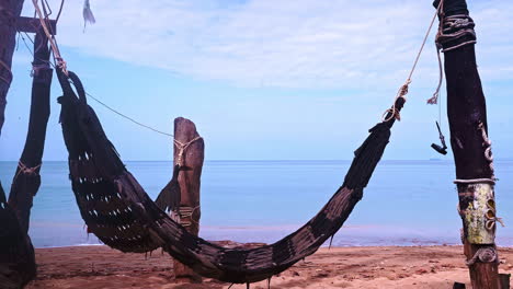 Handmade-hammock-hanging-empty-on-sandy-beach-with-view-to-sea-waves