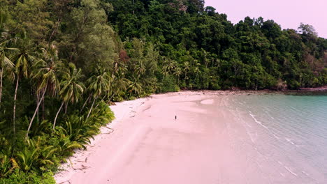 Person-walking-on-tropical-Koh-Kood-beach-with-palm-jungle-in-lagoon