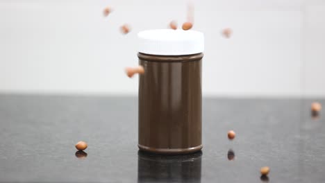 Bottles-of-chocolate-flavored-peanut-butter-surrounded-by-raw-peanuts-falling-in-slow-motion