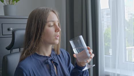 Girl-drinking-clear-water-from-glass,-while-working-in-home-office