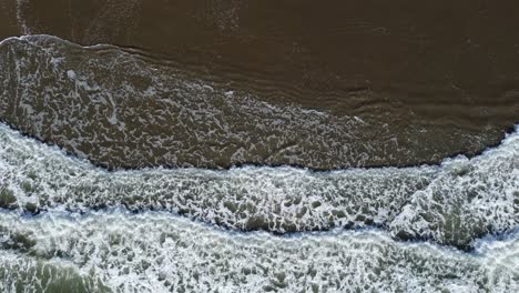 Top-shot-of-incoming-waves-covering-whole-frame-in-full-width-at-shallow-coast-with-sand-beach