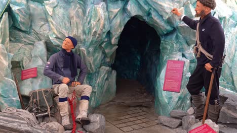 Artificial-glacier-cave-with-two-mannequins-standing-outside---Approaching-dark-cave-opening-at-Norwegian-glacier-museum-in-Fjaerland