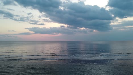 Cloudy-sunset-evening-at-sea-with-calm-waves-and-sky-reflections-in-the-water