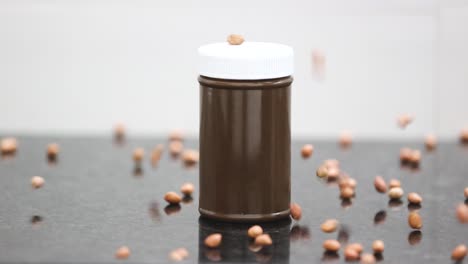 Slow-motion-scene,-bottles-of-chocolate-flavored-peanut-butter-surrounded-by-raw-peanuts-falling-in-slow-motion