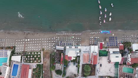 Luftaufnahme-Von-Oben-Nach-Unten-Auf-Den-Strand-Von-Laganas,-Die-Insel-Zakynthos,-Griechenland,-Sonnenschirme-Und-Gebäude-Am-Wasser