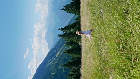 Slow-motion-shot-of-happy-girl-in-white-dress,-walking-and-jumping-in-green-pasture-on-hill-during-sunny-summer-day---tracking-shot