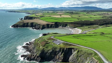 Ireland-Coast-aerial-establishing-shot-of-The-Copper-Coast-drive-road-dropping-into-Kilmurrin-Cove-winding-its-way-to-the-Comeragh-Mountains-on-a-summer-morning