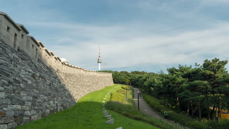Menschen,-Die-In-Der-Nähe-Der-Stadtmauer-Von-Seoul-Im-Namsan-Park-Und-Des-Seoul-Turms-Am-Namsan-Berg-Im-Hintergrund-In-Südkorea-Spazieren-–-Zeitraffer-Im-Sommer