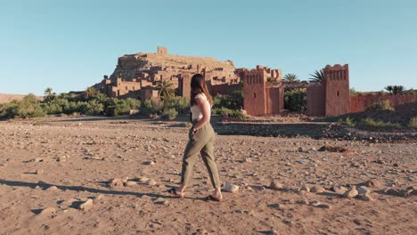 Young-caucasian-woman-walking-in-front-of-Ait-Ben-Haddou-fortress-in-Morocco