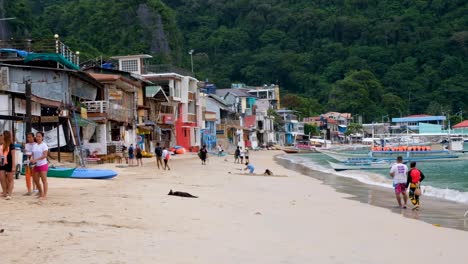 White-sandy-beach-lined-with-cafes,-restaurants-and-bars-with-crowds-full-of-tourist-and-Filipino-people-in-El-Nido,-Palawan,-Philippines