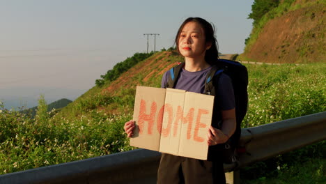 young-Asian-hitchhiker-wanting-to-go-home-with-a-sign-stating-her-destination-of-travel