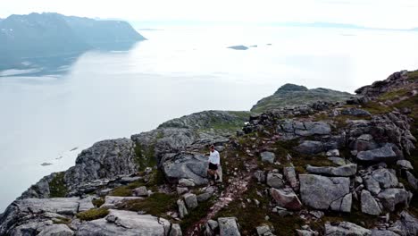 Aerial-View-of-A-Man-Walking-On-The-Peak-of-Salberget-Hill-in-Flakstadvag,-Norway